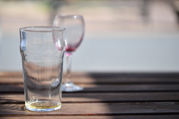 An empty water glass in front of an empty wine glass. Both are placed on wooden table.