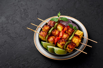 Paneer Tikka at skewers in black bowl at dark slate background. Paneer tikka is an indian cuisine dish with grilled paneer cheese with vegetables and spices. Indian food. Copy space