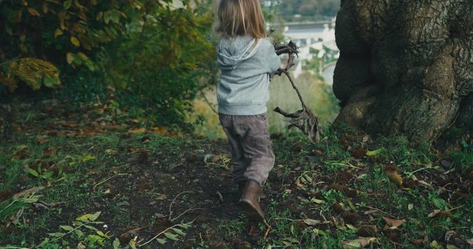 Little toddler with a stick is walking in the woods