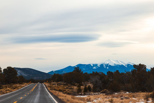 Amazing winter scenery, empty expressway US 89 N towards, Flagstaff, AZ, Snow covered San Francisco peak at the backdrop with awesome lenticular clouds over the mountains. Long drive/road trip travel 