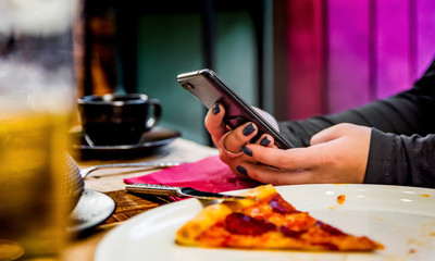 woman hand using mobile phone in cafe with a piece of pizza in plate on table