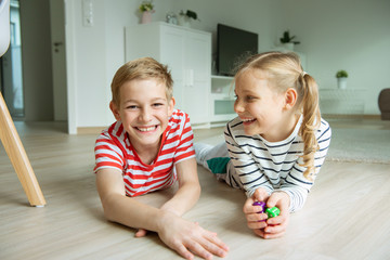 Portrait of two cheerful children laying on the floor and playing with colorful dices