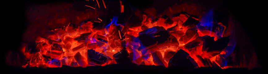 Fototapeta premium Hot wooden coals in the dark. Grill with hot coals and beautiful magic sparks with blue flame