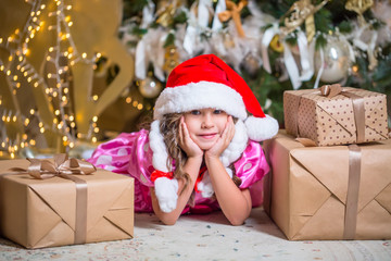 Smiling cute little girl near with santa hat near gifts and Christmas tree. New year or Christmas celebration at home