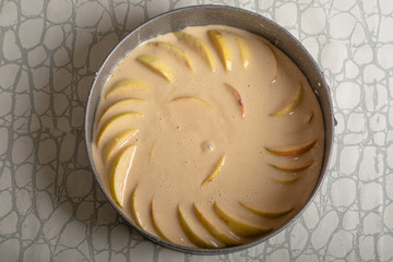 adding dough to a baking dish in which apple slices are already laid out. making apple pie. view from above