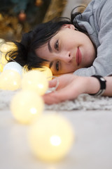 Fototapeta na wymiar Happy attractive brunette girl lying at home with a garland of lights, selective focus