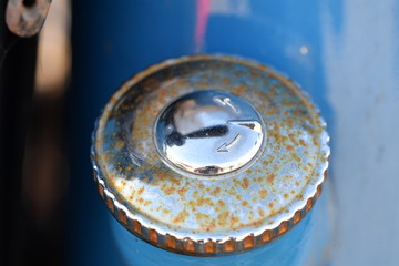 A rusty filler cap of an old, blue motorcycle.