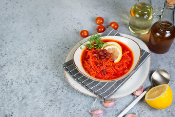 Traditional Ukrainian borsch with  red beans in a white plate stands on a gray concrete background. Top view with copy space.