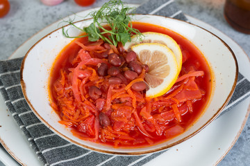 Ukrainian vegetarian borscht with red beans in a white plate stands on a gray concrete background.