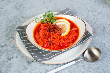 Ukrainian vegetarian borscht with red beans in a white plate stands on a gray concrete background. Top view