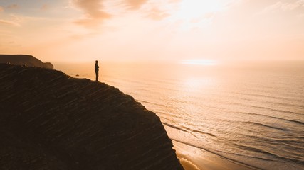Beautiful view of a person standing on a cliff over the ocean at sunset in Algarve, Portugal