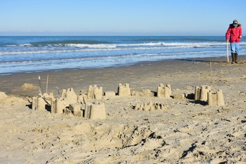  sand castle on the north sea beach in belgium and  person with red jacket and shovel