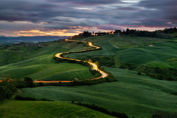 Fototapeta premium Kręta droga, światła samochodów, zachód słońca w tle, Toskania, Włochy