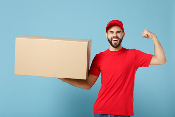 Delivery man in red uniform isolated on blue background, studio portrait. Male employee in cap t-shirt print working as courier dealer hold empty cardboard box. Service concept. Mock up copy space.