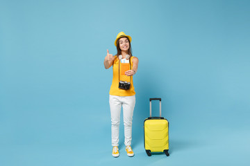 Traveler tourist woman in yellow summer casual clothes hat hold tickets bag camera isolated on blue background. Female passenger traveling abroad travel on weekends getaway. Air flight journey concept