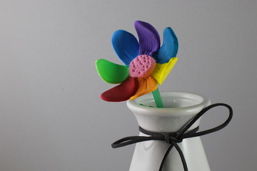 A multi-colored flower made of plasticine, stands in a white vase