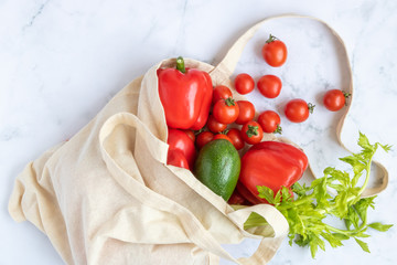 Linen bag reusable with vegetables: avocado, celery, red bell pepper, cherry tomatoes on a marble background. Concept - a world without plastic.