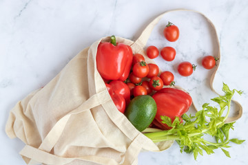 Linen bag reusable with vegetables: avocado, celery, red bell pepper, cherry tomatoes on a marble background. Concept - a world without plastic.