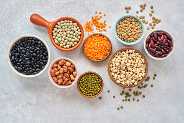 Legumes and beans assortment in different bowls on light stone background . Top view. Healthy vegan...