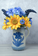 Fototapeta na wymiar Bouquet of sunflowers and blue flowers in an old antique vase on a grey background