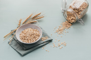 bowl of dry oat flakes with ears of wheat on light background. Cooking oats porridge concept top view - obrazy, fototapety, plakaty