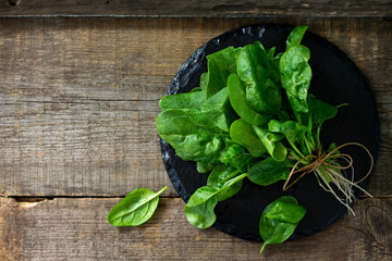 Leaves of fresh baby spinach on a rustic wooden table. Top view flat lay background with copy space.