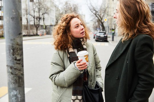 Two Young Girls Seriously Talking On The Street In The Morning In Autumn With A Cup Of Coffee