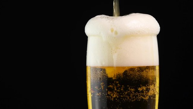 Close up pouring lager beer in glass over black