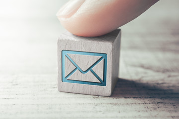 Macro Of An E-Mail Icon On A Wooden Block Arranged By A Female Finger On A Table