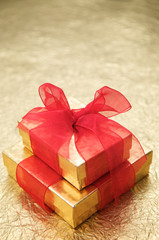 Two gold gift boxes with red ribbons stacked on textured metallic gold background with copy space