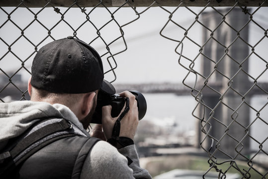 male photographer with camera and cap behind fence in New York City