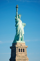 Full length view of the Statue of Liberty standing against bright blue sky on a clear sunny summer day in New York City, USA