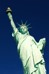 Fototapeta premium Statue of Liberty standing in a frontal three-quarter diagonal view in bright sun against deep blue sky