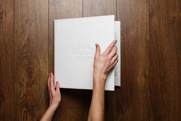 Obraz premium golden stylish square gift cardboard box for photo album. leather family photo book in the open box..the person is looking at photo book.womans hand open bright original box for white wedding album.