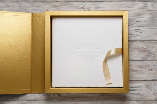 golden stylish square gift cardboard box with lid for photo album. Bright original box for wedding photo album with white leather cover. leather family photo book in the open box with lid and ribbon..