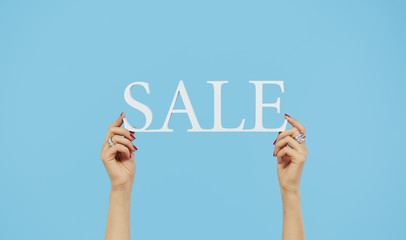 Fototapeta premium Female hands hold a sign with the inscription sale on a blue isolated background. Christmas and holiday sales concept