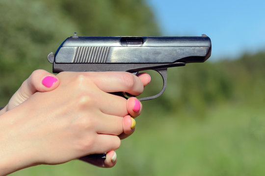 a woman with a beautiful manicure aims a combat pistol and is ready to make a shot. concept of female self-defense and violence, protection from maniacs and rapists.