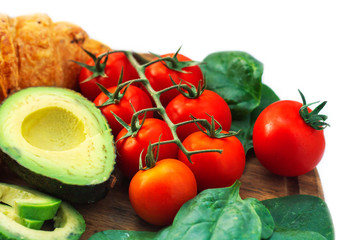 Healthy food background with various vegetables ingredients like tomatos, avocado, meat, cheese, spinah and fresh croissants.