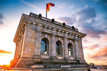 German flag waving on top of Reichstag (Bundestag) building against dramatic sky during sunset, Berlin, Germany © golovianko