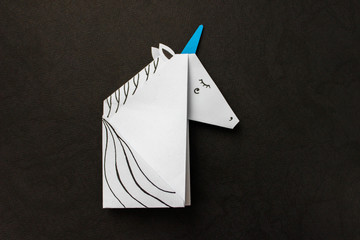 White unicorn made in the origami technique on a black background. © Maria S