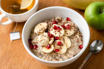 Porridge oats or oatmeal in bowl with banana slice, pomegranate seeds and flax seeds on a wooden table background. Selective focus. Healthy breakfast, healthy lifestyle, dieting concept