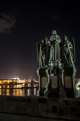 Statue On Charles Bridge And View Over Moldova River And Illuminated Buildings In Prague In The Czech Republic