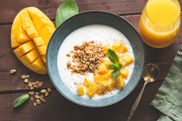 Yogurt bowl with mango and breakfast cereals oat granola on a wooden table. Top view. Toned image. Concept of dieting, weight loss, healthy eating and healthy lifestyle