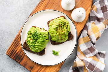 Vegan avocado toast with rye bread on a white plate, table top view
