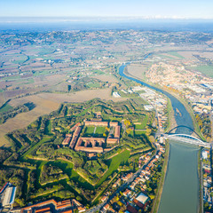 Aerial view of modern six-star hexagon shaped fort Cittadella of Alessandria on winding river Tanaro. Piedmont, Italy. Alps in the background. Bridge Ponte Meier connects fortress to town centre