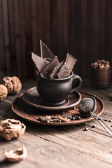 Pieces of chocolate broken in a cup and nuts on a wooden table. A set of ingredients for making hot chocolate.