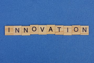 The word innovation made of brown wooden letters lies on a blue table