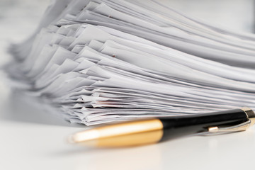 A pile of paper sheets on a white table on a wooden table with a golden pen