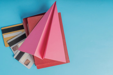 Red passports with credit cards lie on a blue background under a pink paper airplane