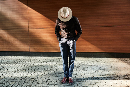 A man in a hat stylish standing on a street on block pavement at wooden wall on 